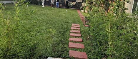 A pathway leading to a building with a tiled roof and a small garden area with grass and plants.