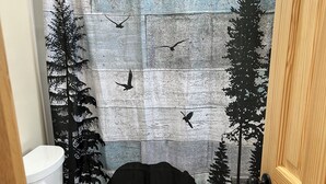 A bathroom with a shower curtain depicting a forest scene, a toilet, and a rug. - One room guest house with hot tub, three twin beds, one futon, kitchen, bathroom (Collbran)
