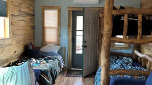 A cozy cabin-style room with two beds, a wooden ceiling, and a dog resting on a rug. - One room guest house with hot tub, three twin beds, one futon, kitchen, bathroom (Collbran)