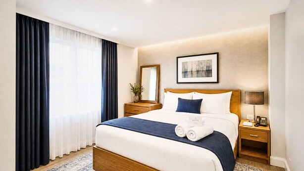 A hotel room with a large bed, a bedside table with a lamp, a mirror, and a framed picture on the wall.