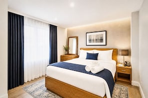 Una habitación de hotel con una cama grande, una mesita de noche con lámpara, un espejo y un cuadro en la pared.