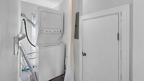 A laundry room with a stacked washer and dryer, a ceiling fan, and a door.