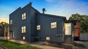 A two-story residential building with a dark gray exterior, multiple windows, a satellite dish, and a small attached garage.