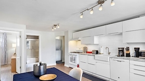A modern kitchen with white cabinets, a stove, and a dishwasher. There is a dining area with a table and chairs.