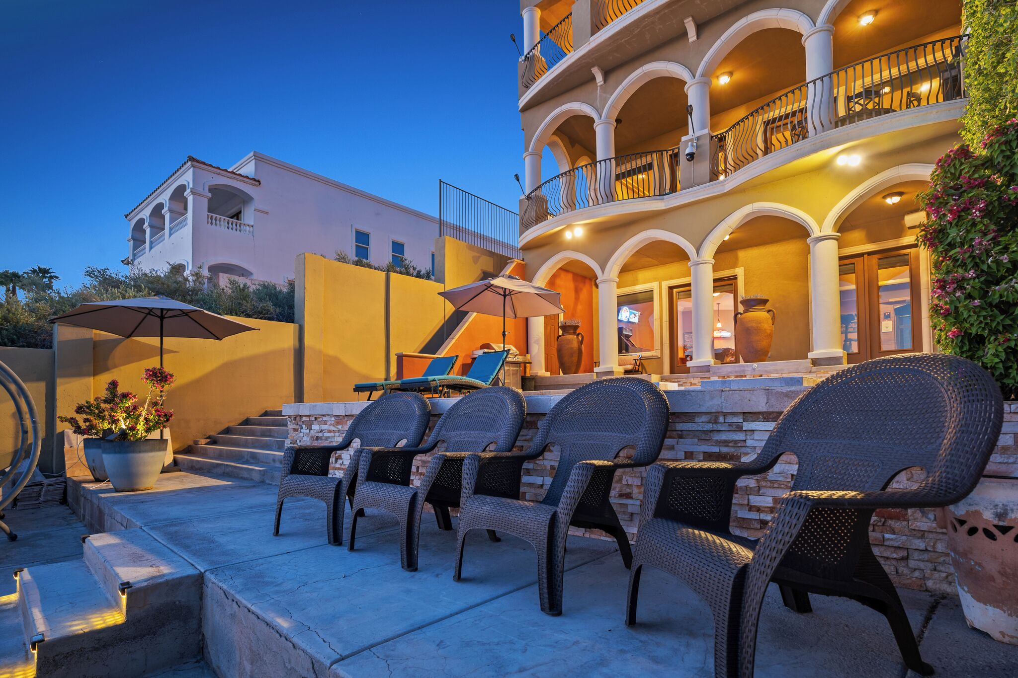 A multi-story building with a balcony, outdoor seating area with wicker chairs, and a potted plant.