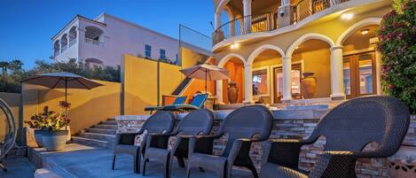 A multi-story building with a balcony, outdoor seating area with wicker chairs, and a potted plant.