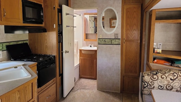 A compact kitchen with wooden cabinets, a microwave, a stove, and a refrigerator. - The Riverside Fleetwood.   (Petit Étang)