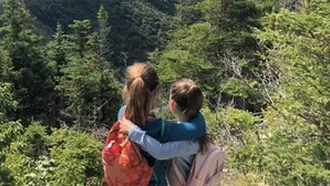 Two people embracing on a mountain trail with a view of a forested landscape and a distant body of water. - The Riverside Fleetwood.   (Petit Étang)