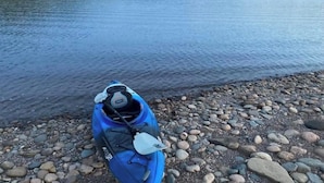 A kayak on a rocky shore by a calm lake with hills in the background. - The Riverside Fleetwood.   (Petit Étang)