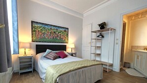 Un dormitorio con cama, mesitas de noche, un cuadro, un armario y una pequeña estantería.