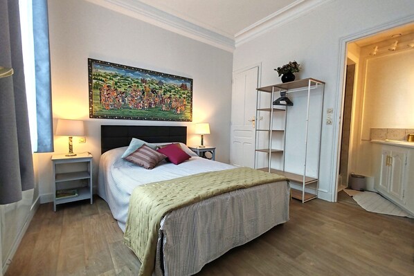 A bedroom with a bed, bedside tables, a painting, a wardrobe, and a small shelf. - Appartement Le Baron Cœur de Rouen Avec Petit Déjeuner Inclus - Normandie (Rouen)