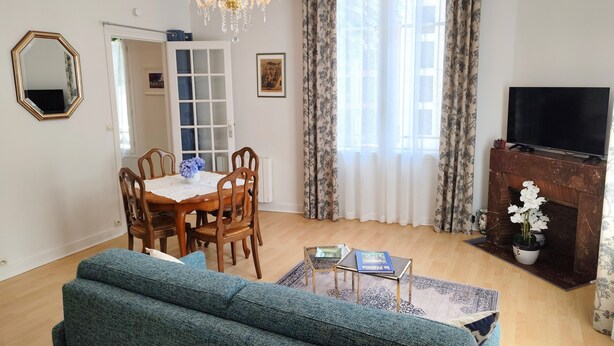 Una sala de estar con un sofá, una mesa de comedor con sillas, una araña, una chimenea y un televisor.