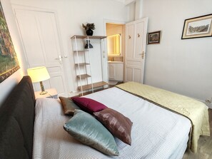 A bedroom with a bed, pillows, a nightstand, a lamp, a wardrobe, and a mirror. - Appartement Le Baron Cœur de Rouen Avec Petit Déjeuner Inclus - Normandie (Rouen)