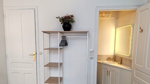 Un baño con tocador, espejo y estante con un jarrón de flores.