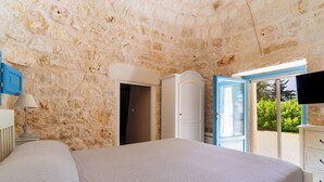A bedroom with a stone wall, a bed, a wardrobe, and a TV.