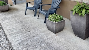 Una casa de fachada de piedra, con escalones y dos sillas Adirondack en un patio de concreto con macetas.