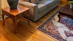 A cozy living room with a grey sofa, two wooden side tables with lamps, a patterned rug, and a wooden cabinet with books and decorative items. - Cozy Home near the Beach, with Hiking & Biking Trails, Wineries & Restaurants (St. Williams)
