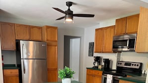 Una cocina moderna con gabinetes de madera, electrodomésticos de acero inoxidable, una isla verde con taburetes de bar y un ventilador de techo.