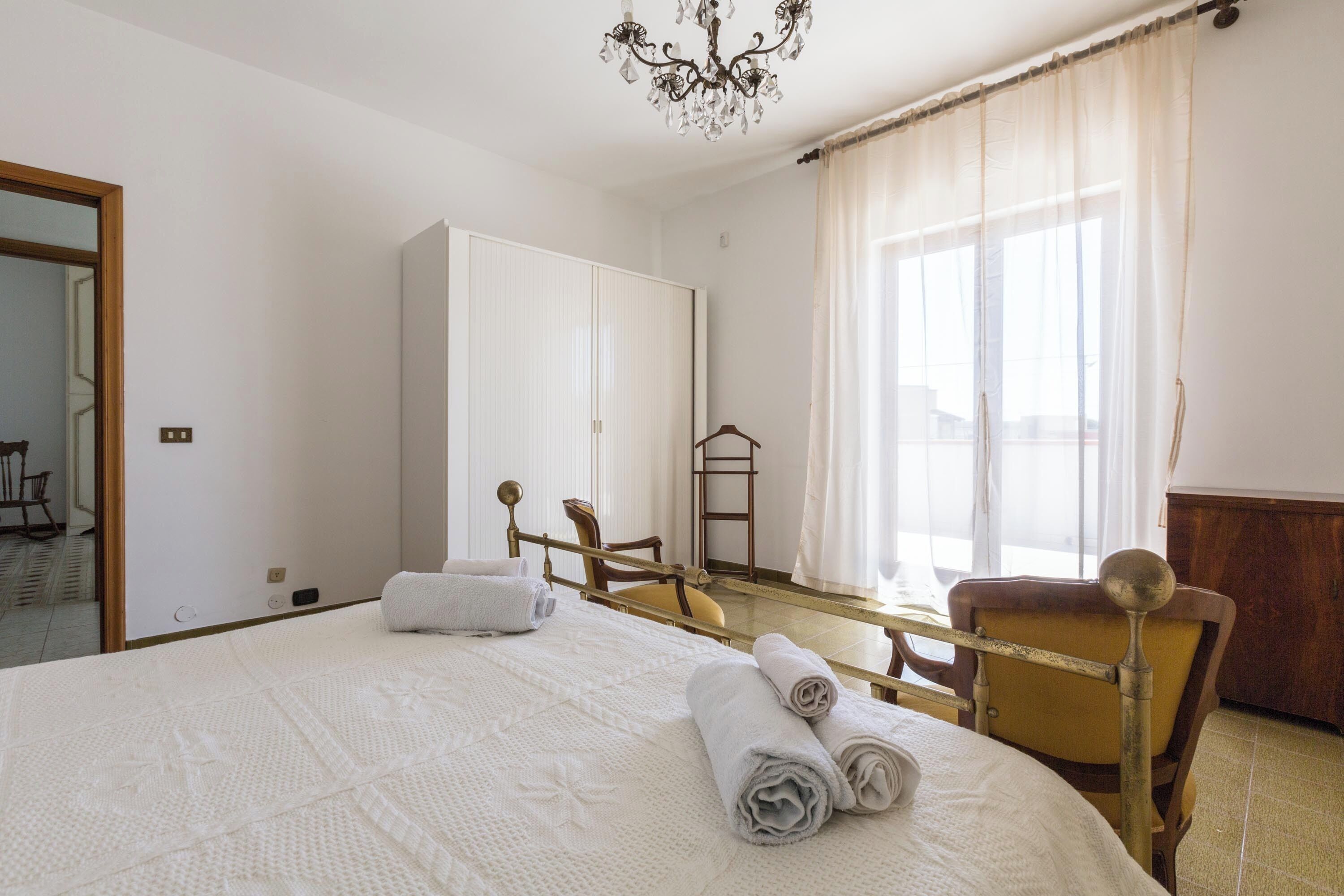 A hotel room with a large bed, a wooden chair, a wardrobe, and a mirror.
