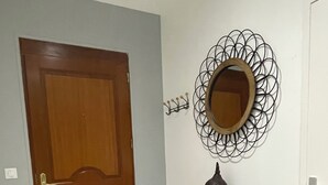 Un corridoio con una porta in legno, un tavolo consolle in metallo nero con un vaso, uno specchio decorativo e un tappeto a motivi.