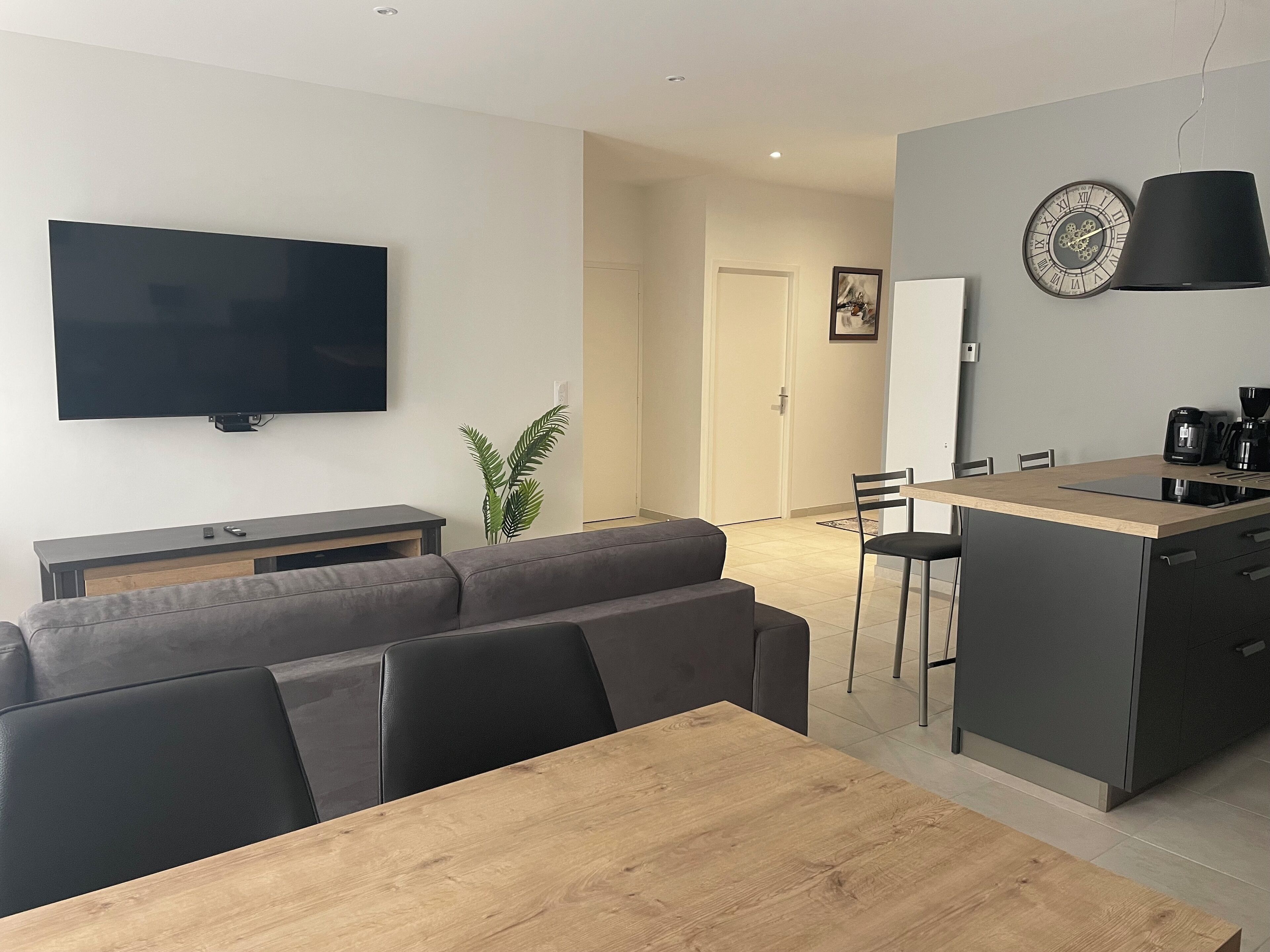 A modern living space with a flat-screen TV, a sofa, a dining table, and a kitchen area with a coffee maker.