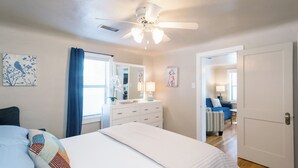 Un dormitorio con cama, cómoda, ventilador de techo y puerta que da a otra habitación.