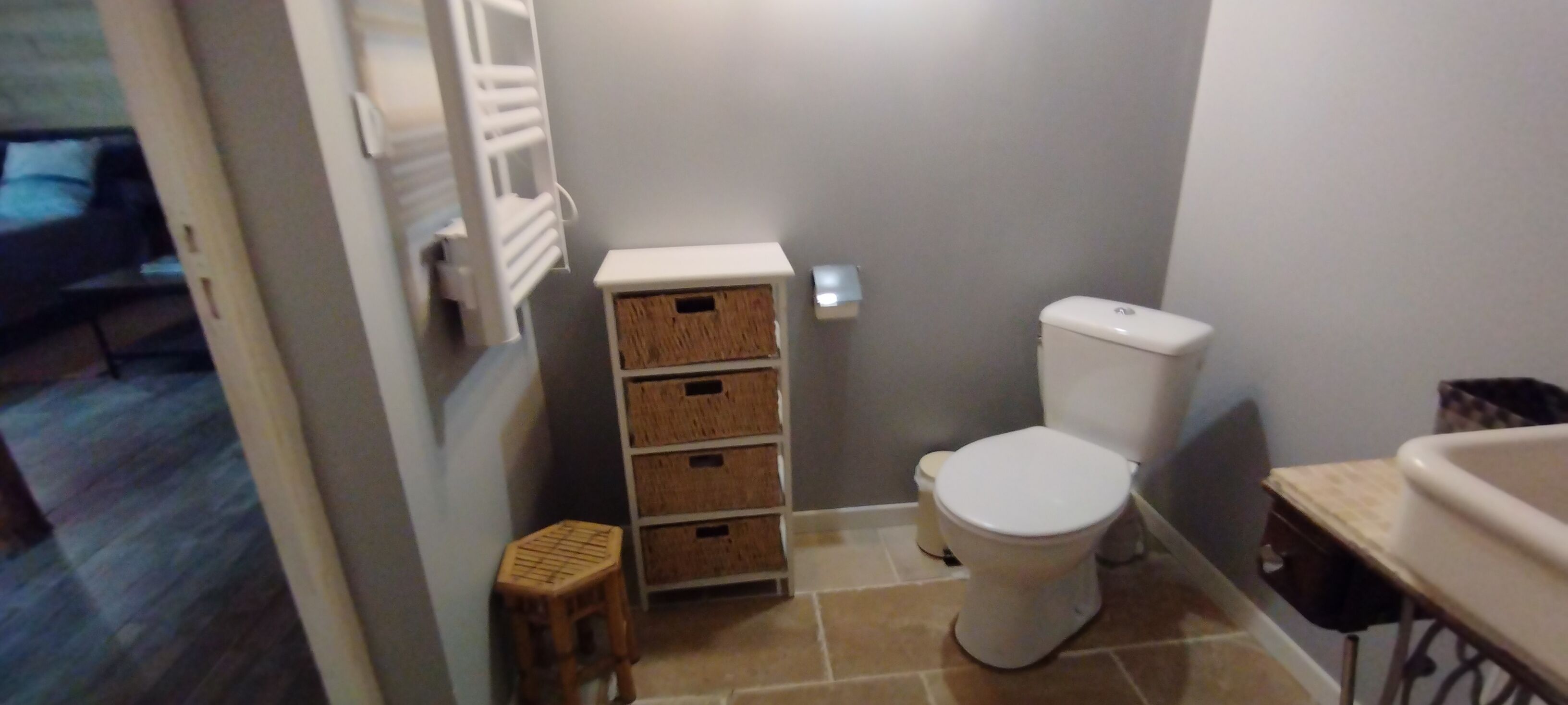A bathroom with a toilet, a small stool, and a storage unit with baskets.