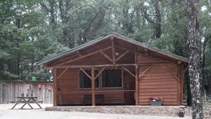 A rustic wooden cabin with a porch, a picnic table, and a bench.