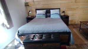 A wooden-paneled room with a bed, two bedside tables, a bench, and a sofa.