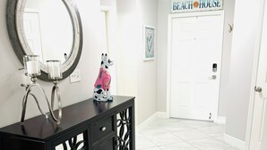 A hallway with a black console table, a round mirror, and a decorative dog statue. A door labeled "Beach House" is visible in the background. - Perfect Getaway! Naples, Walk To Vanderbilt Beach -Immaculate! (Naples)