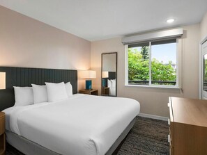 Une chambre d’hôtel avec un grand lit, des tables de chevet, un miroir et une fenêtre donnant sur un paysage verdoyant.