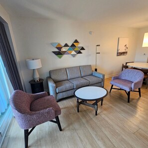 Un salon moderne avec un canapé gris, deux fauteuils, une table basse et une œuvre d’art murale.