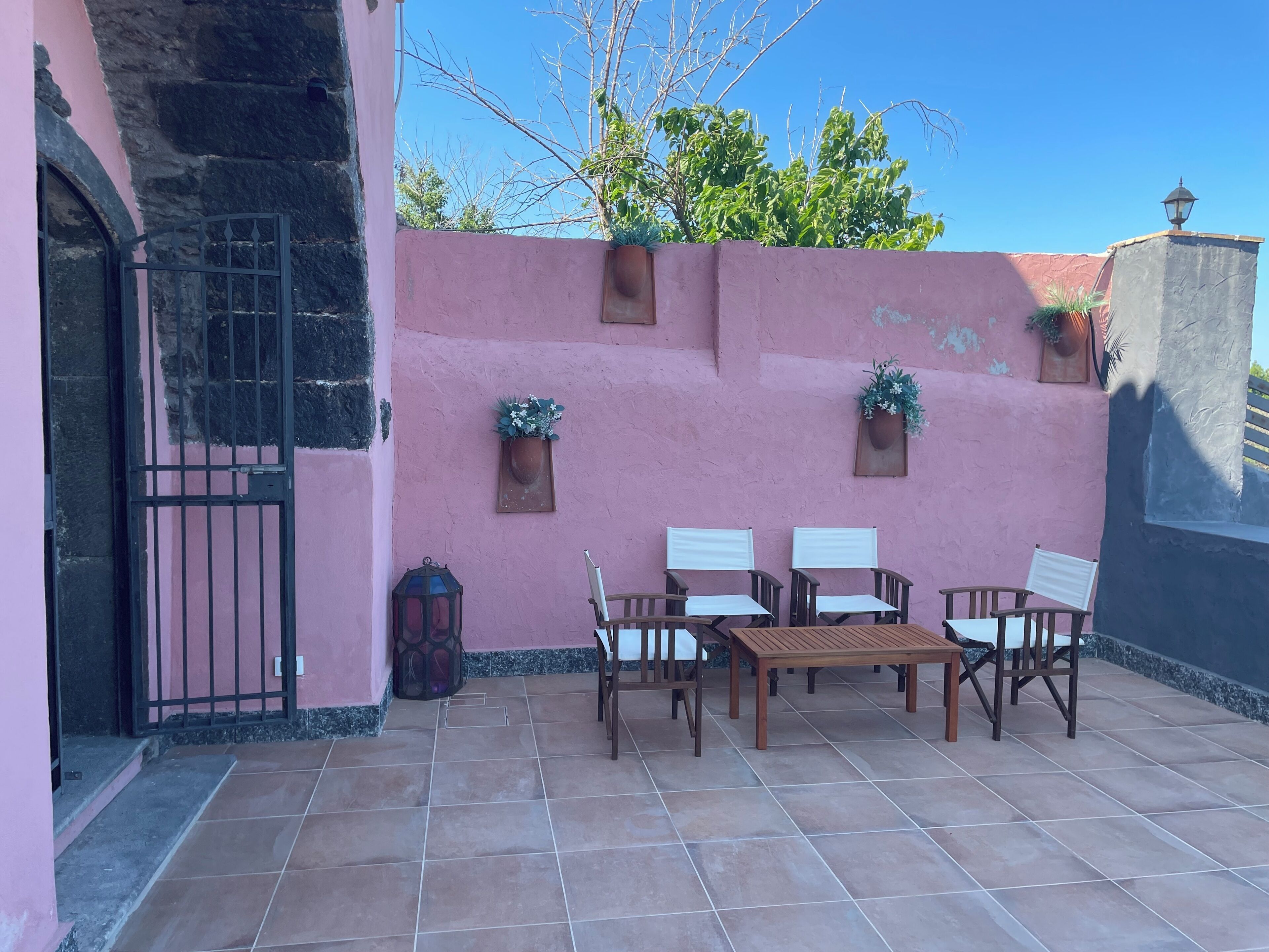 A patio with a pink wall, a tiled floor, and a wooden table with chairs.