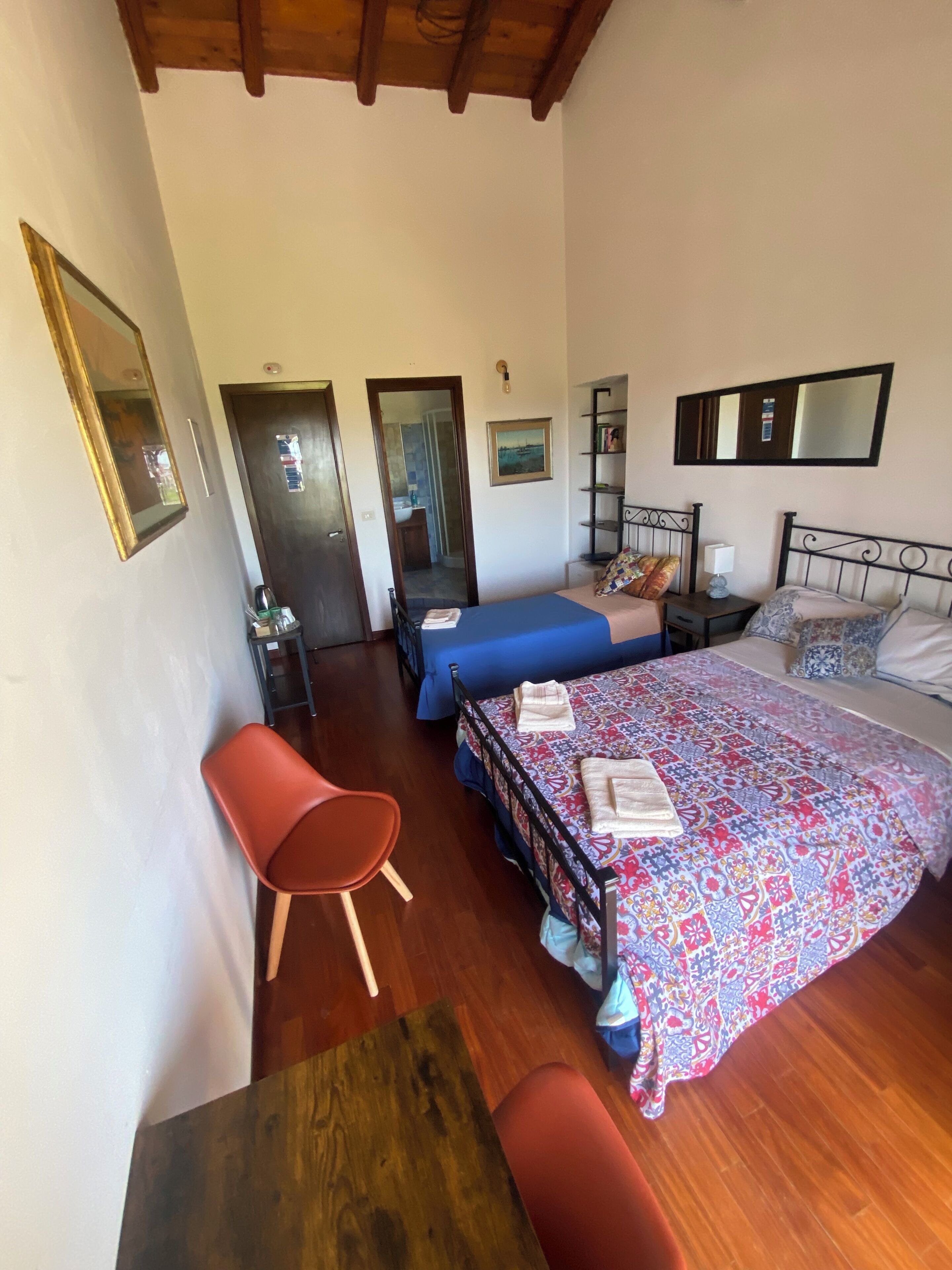 Een slaapkamer met twee bedden, een houten vloer, een rode stoel, een kleine tafel en een deur naar een badkamer.