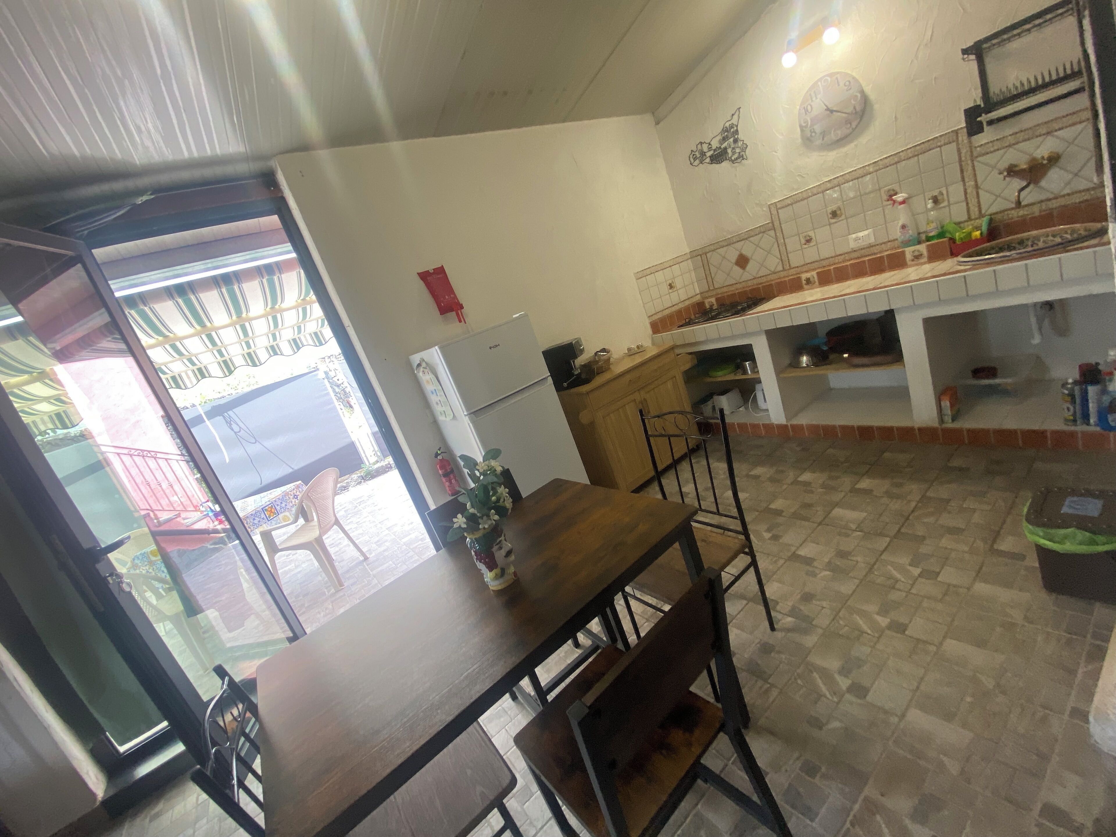 Uma sala de jantar com uma mesa e cadeiras de madeira, uma geladeira e uma cozinha com fogão e armários.