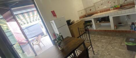 Uma sala de jantar com uma mesa e cadeiras de madeira, uma geladeira e uma cozinha com fogão e armários.