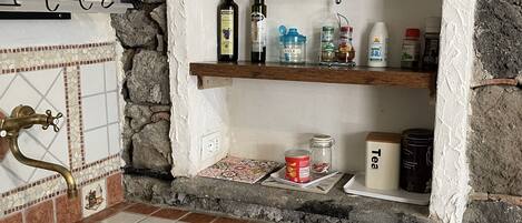 Un baño con pared de piedra, lavabo con azulejos, repisas con artículos de aseo y un perchero.