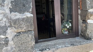 A stone wall with a window revealing a room with a dining table and chairs. - Le Decime Retreat (Mascali)