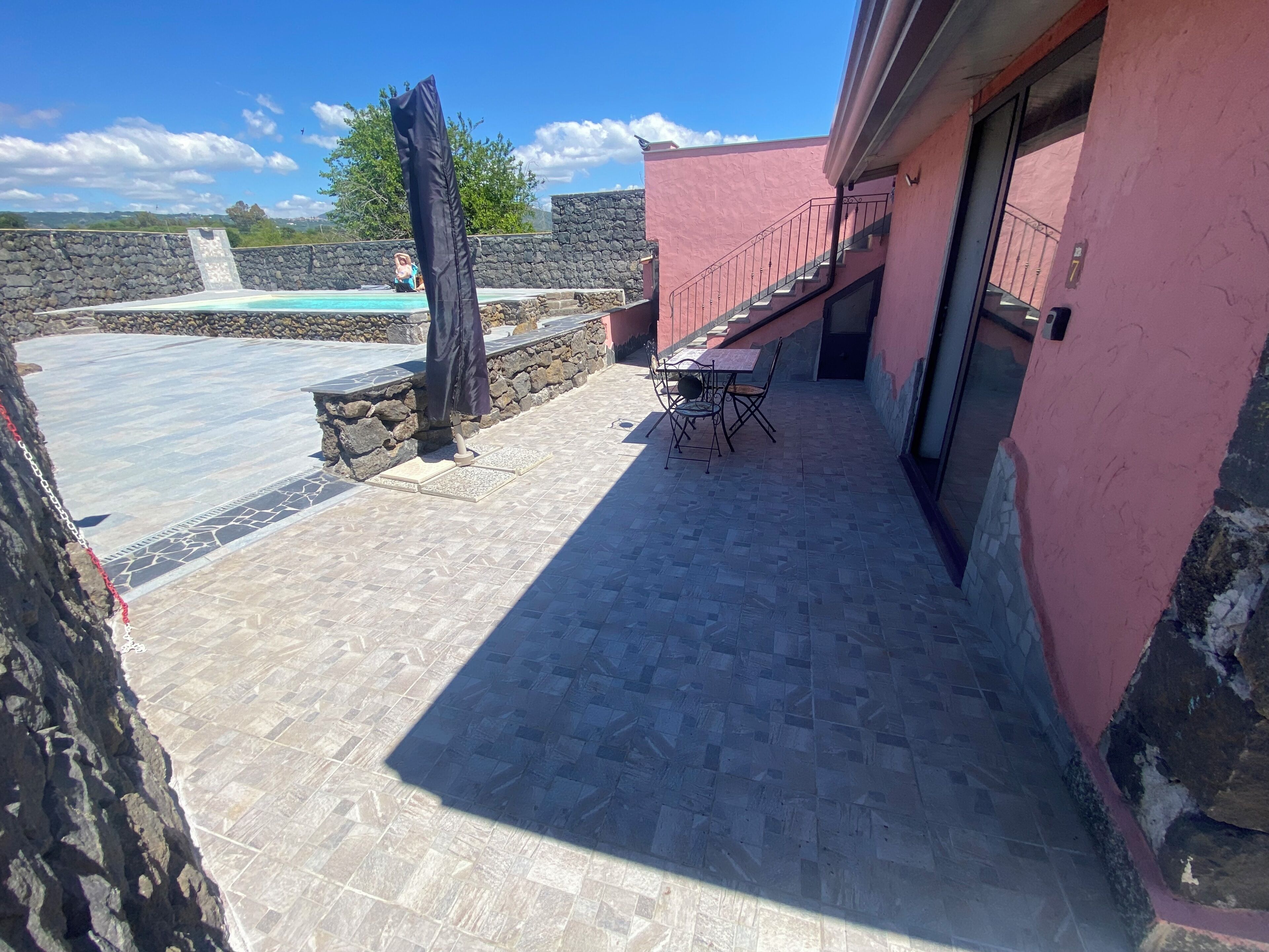 A patio area with a pool, stone wall, and a table with chairs.