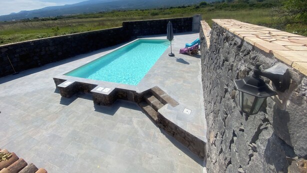 A rectangular swimming pool with stone walls, a stone deck, and a view of distant mountains. - Le Decime Retreat (Mascali)