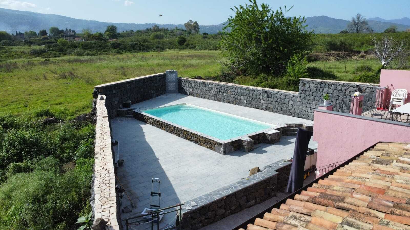 A rooftop swimming pool with stone walls, a chair, and a table.