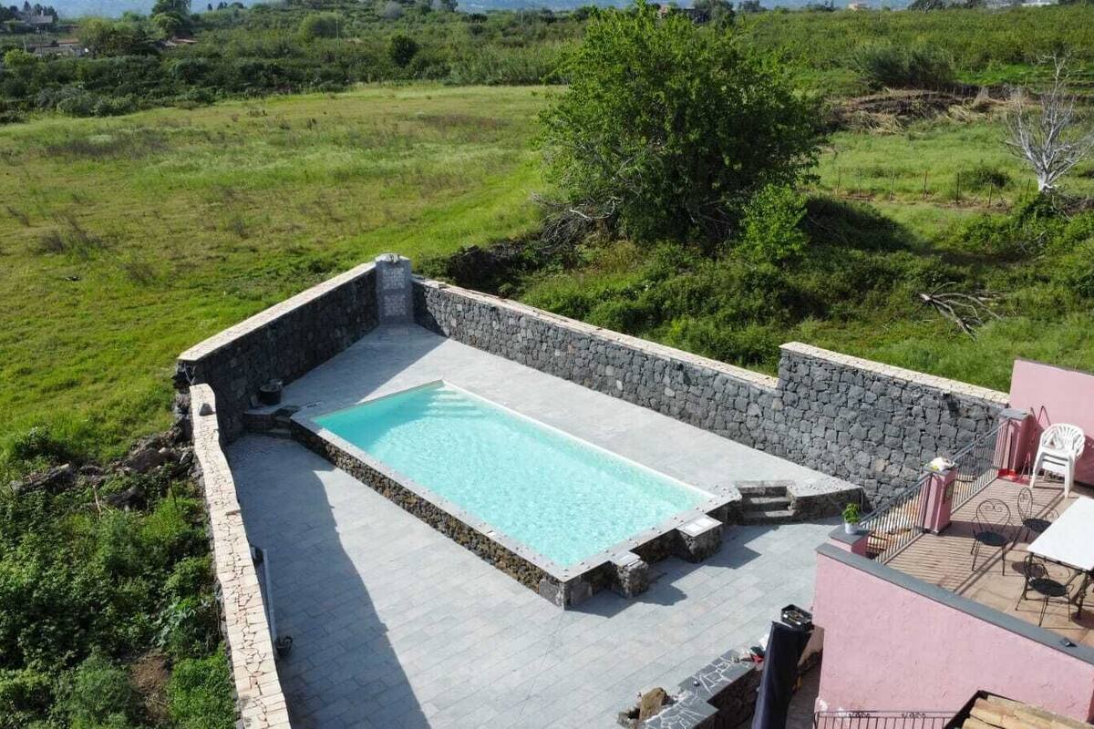 Una piscina en la azotea con muros de piedra, rodeada de un paisaje con césped.