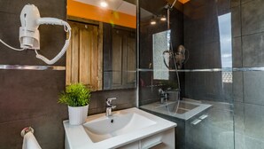 Une salle de bain moderne avec un lavabo blanc, un sèche-cheveux fixé au mur et un espace douche.