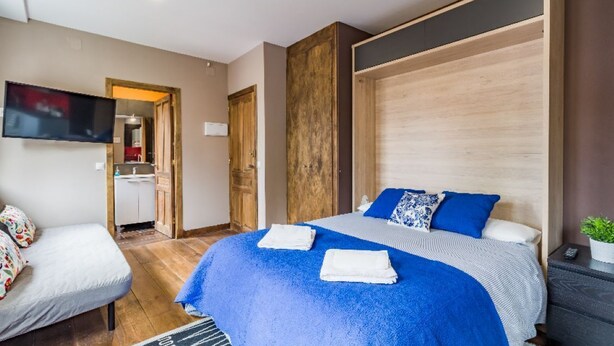 Une chambre d’hôtel moderne dotée d’un grand lit, d’un téléviseur fixé au mur, d’une petite kitchenette et d’une armoire en bois.