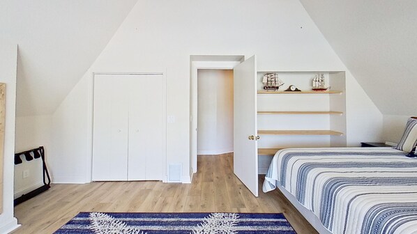 A bedroom with a sloped ceiling, a bed with striped bedding, a wooden floor, a blue and white rug, and a shelf with model ships. - The Hydeaway! Waterfront, Docks, Ice Machine, Kayaks, by King Springs (Crystal River)
