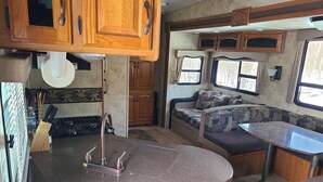 A compact RV kitchen with a granite countertop, wooden cabinets, and a built-in seating area with a patterned cushion. - Riversides Copper Canyon! (Petit Étang)