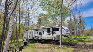 A recreational vehicle (RV) parked in a wooded area with a clear sky. - Riversides Copper Canyon! (Petit Étang)