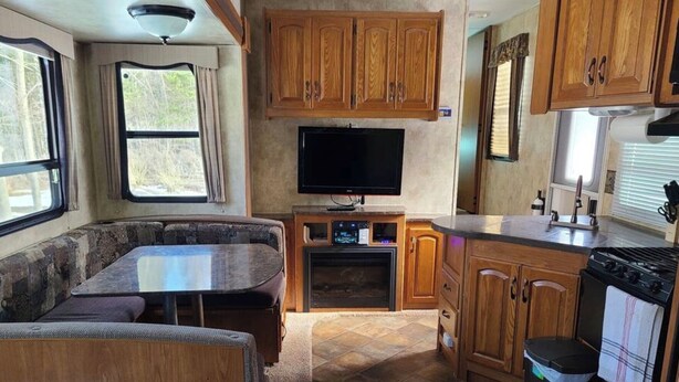 A compact RV kitchen with wooden cabinets, a TV, and a dining area with a table and bench. - Riversides Copper Canyon! (Petit Étang)
