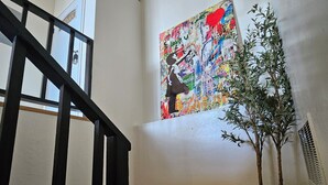 Un escalier avec des rampes en bois, un grand tableau abstrait accroché au mur, une plante en pot et un tapis blanc et moelleux sur le sol.