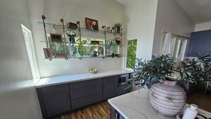 Une cuisine moderne avec des meubles de couleur sombre, un plan de travail en marbre et une étagère en verre où sont exposés des objets décoratifs.